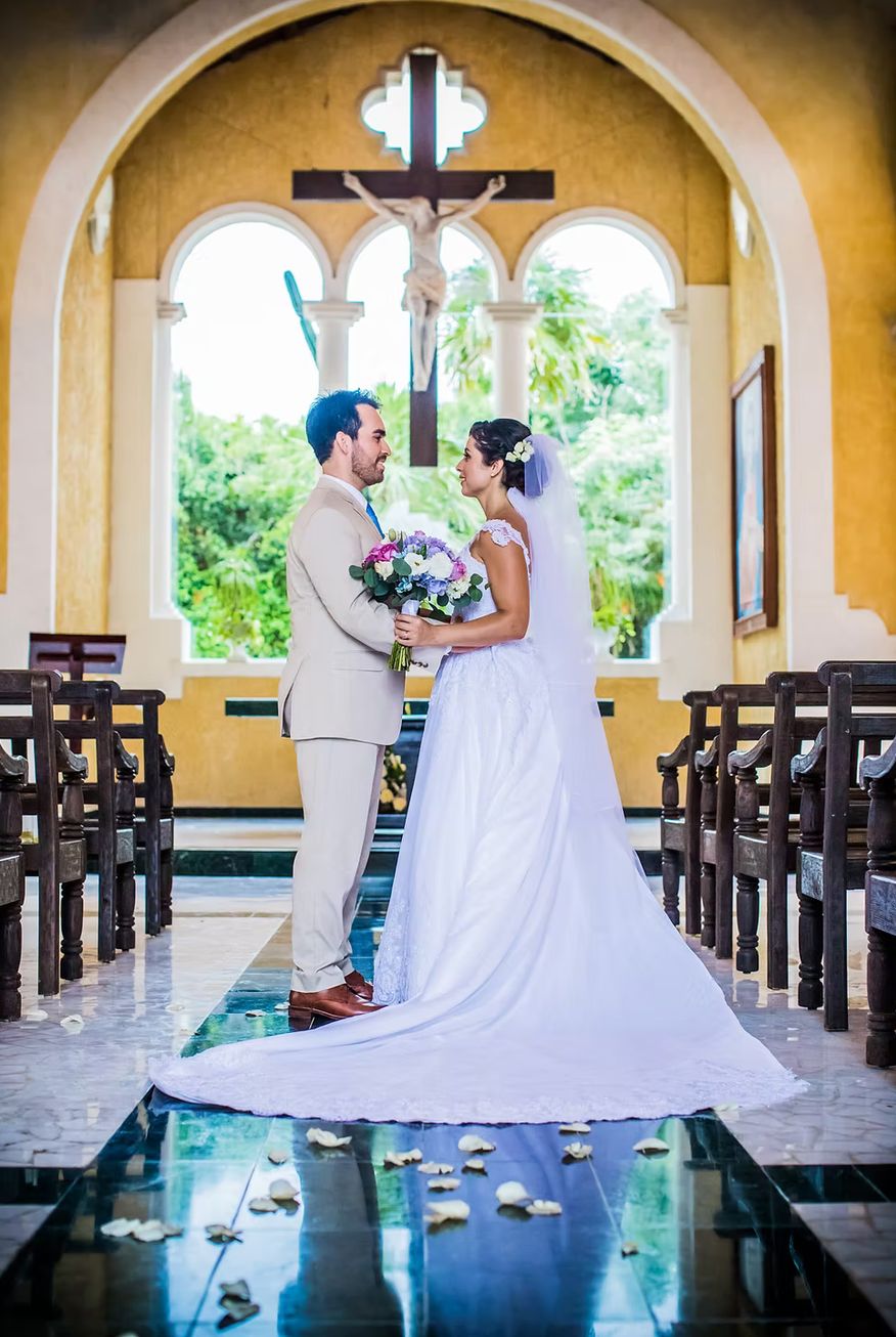 Bride and groom facing each other at the altar of a golden chapel with rose petals on the aisle — destination wedding photography by Murrieta Media